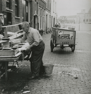 875240 Portret van Piet Schoonhoven ('Piet 't Joodje') die zijn viskar aan het schoonmaken is op de Kroonstraat in Wijk ...
